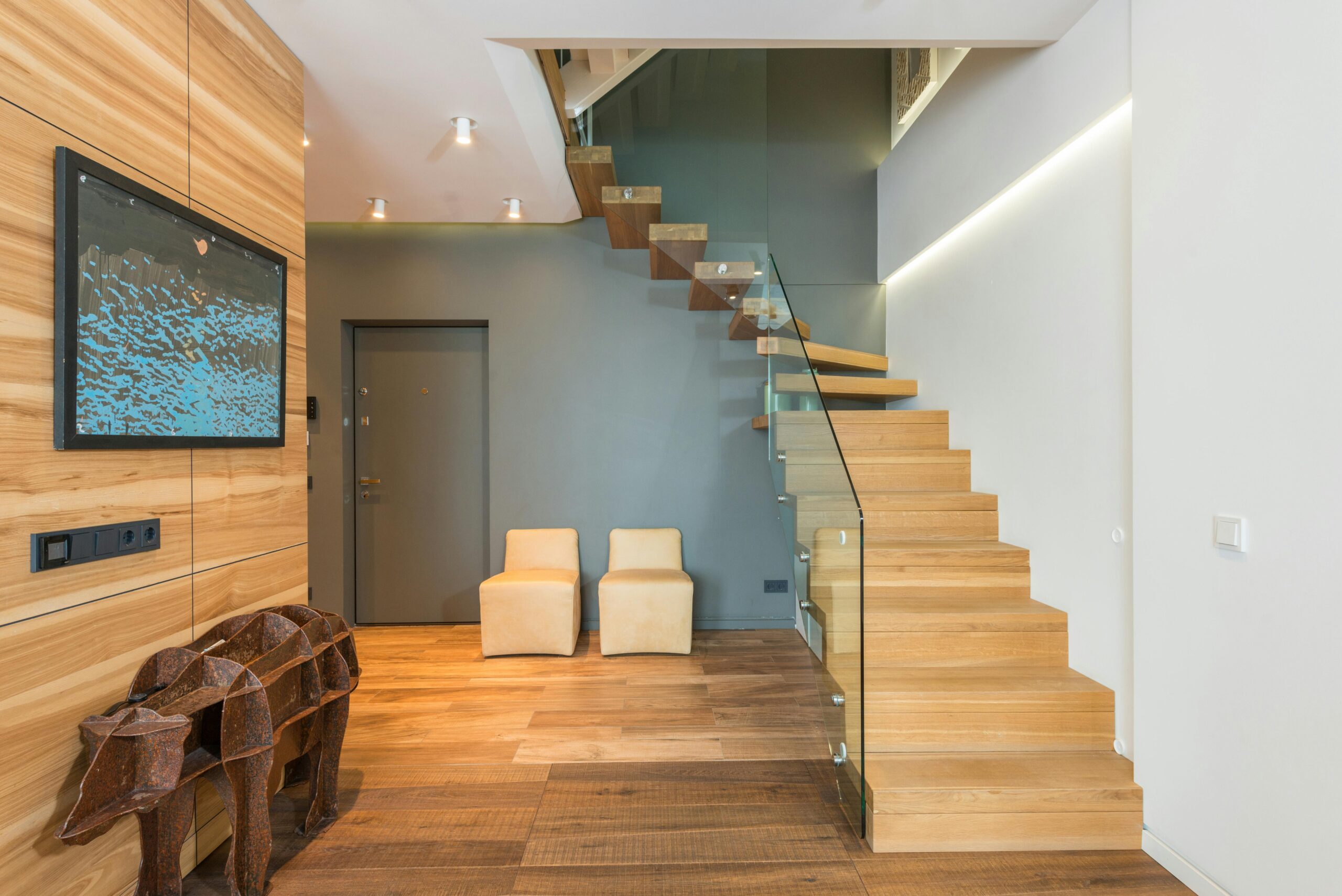 Contemporary stylish house hallway interior with creative statue under TV set cozy chairs and wooden stairway